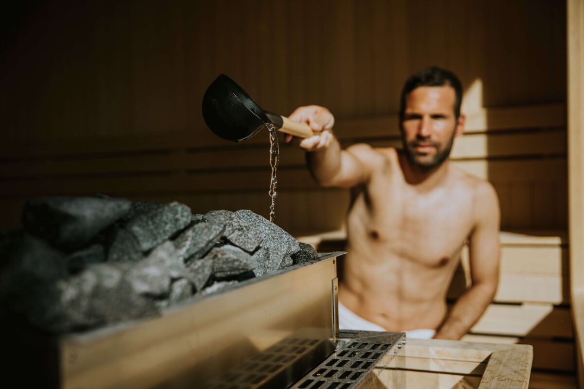 man in sauna pours water over rocks